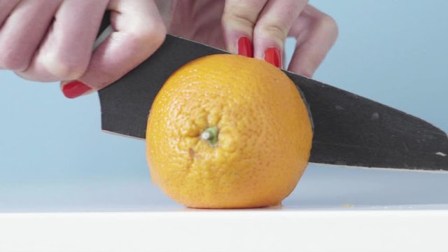 Mano con smalto rosso che taglia arancia a met&agrave; con coltello