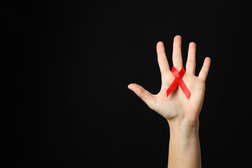 Hand and red awareness ribbon against black background, space for text