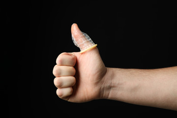 Hand and condom on black background, space for text