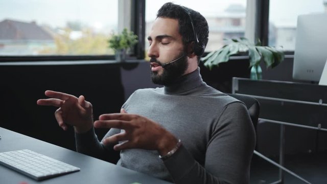 Office technical support talking with customer on wireless headset microphones consulting sitting at desktop computer. Modern workspace. Customer support.