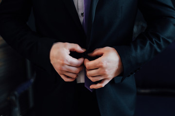 Buttoning a jacket hands close up. Stylish man in suit fastens buttons and straightens his jacket preparing to go out. Preparing for a wedding