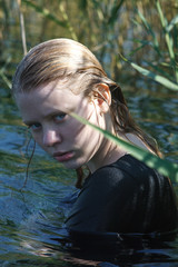 portrait of young girl in black dress with wet long blonde hair posing outdoors
