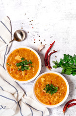 Dal - Traditional spicy Indian soup of red lentils and vegetables in a white bowl and spices on a grey background, top view. Indian and vegetarian food.