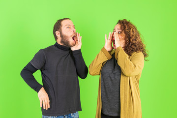 Young beautiful couple over green background, mad, shouting and yelling with aggressive expression.Frustration and crazy concept.