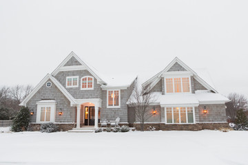Wood shingled home in snow with warm lights illuminating windows - Powered by Adobe
