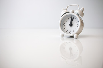 Small analog white clock showing twelve o'clock with a white background.