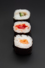 Set of three sushi rolls with fish, avocado and cheese on black background isolated. Traditional japanese food. Asian restaurant meals delivery. Copy space.