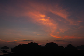 A picturesque sunset over the sea with a dark silhouette of the rocks. Dark cliffs with beautiful pink clouds and light on the sky. Red gleams from the sun in the evening sky.