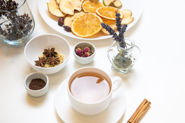 a white mug on a white table with herbal tea and herbal ingredients laid out on the table. Concept on the topic of herbal treatment for colds and flu in autumn