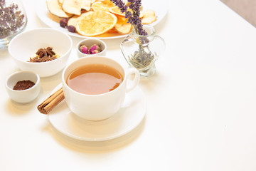 a white mug on a white table with herbal tea and herbal ingredients laid out on the table. Concept on the topic of herbal treatment for colds and flu in autumn