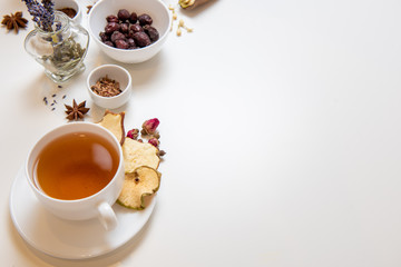 a white mug on a white table with herbal tea and herbal ingredients laid out on the table. Concept on the topic of herbal treatment for colds and flu in autumn