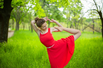 Naklejka na ściany i meble Young sports girl in a red dress practices yoga in a quiet green forest. Meditation and oneness with nature