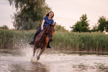 Fototapeta na wymiar A young girl riding a horse on a shallow lake. A horse runs on water at sunset. Care and walk with the horse. Strength and Beauty