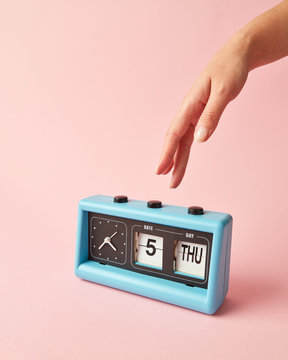 Woman's hand presses on the button on retro flip clock with calendar day thuesday, date 5 on a color of the year 2019 Living Coral pantone background. Place for text.