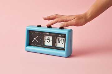 Retro style of flipping clock with calendar on a background color of the year 2019 Living Coral pantone. Girl's hand turns on a buttom on the clock. Place for text.