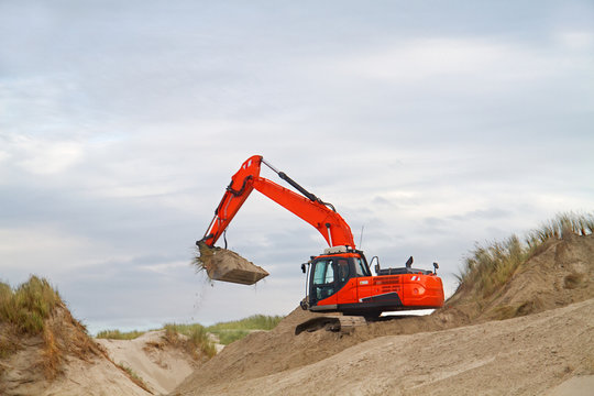 Orange digger working on recovery of dunes after wave attack, the beech of the Dutch island Terschelling