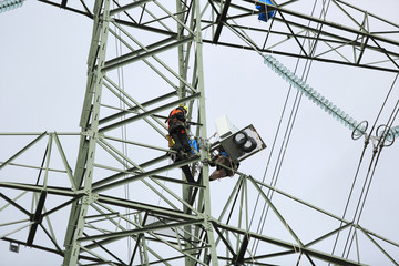 Fototapeta Pracownik na wysokości montuje skrzynię ze sterownikami na słupie wysokiego napięcia.	 obraz