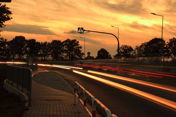 Światła samochodów wieczorem o zachodzie słońca, przejście dla pieszych. - obrazy, fototapety, plakaty