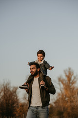 Happy father with son ride on his shoulders on walking in autumn park.