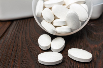 White medical supplement pills in the plastic spoon on wooden background, macro image