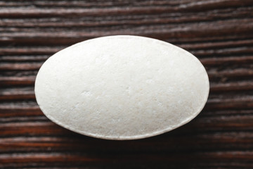 White medical supplement pill on wooden background, macro image, top view