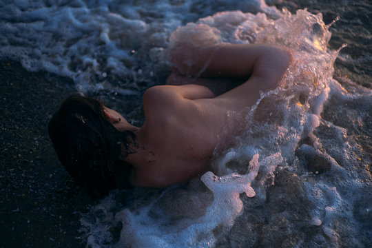 Naked girl lies in the waves of the sea