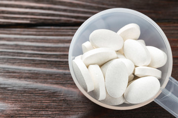 White medical supplement pills in the plastic spoon on wooden background, macro image