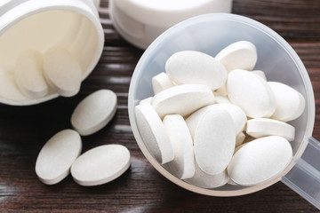 White medical supplement pills in the plastic spoon on wooden background, macro image