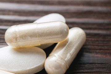 White medical capsules of glucosamine chondroitin, healthy supplement pills on wooden background, macro image