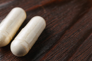 White medical capsules of glucosamine chondroitin, healthy supplement pills on wooden background, macro image