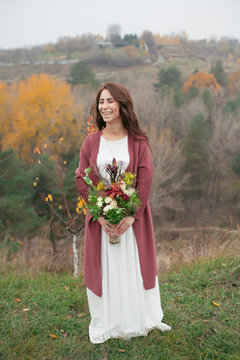 girl in a white dress with a bouquet stands on the background of nature and smiling