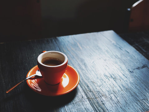 A single shot of espresso in an orange cup on a wooden table
