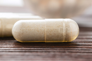 White medical capsules of glucosamine chondroitin, healthy supplement pills on wooden background, macro image