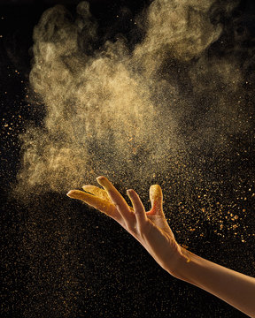 Flying abstract yellow powder cloud with wooman hand against black background