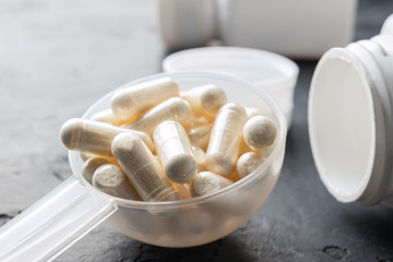 White medical capsules of glucosamine chondroitin, healthy supplement pills in the plastic spoon on dark background, macro image