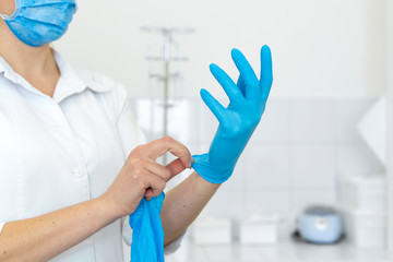 Fototapeta premium A nurse in a white coat puts on rubber gloves before a medical procedure in a bright handling room.