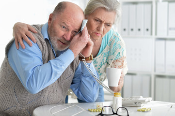 Portrait of sick senior couple calling to doctor