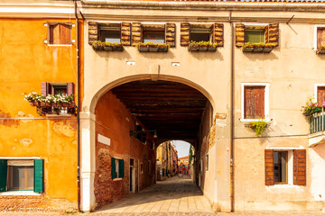 picturesque view at a bright wall with old windows and nice arch leading ti a narrow quiet street, Venice arc , italian archway