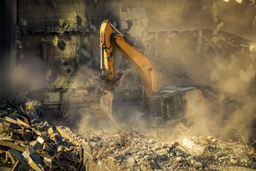 Heavy machinery surrounded with dust  cloud taking down an old building 