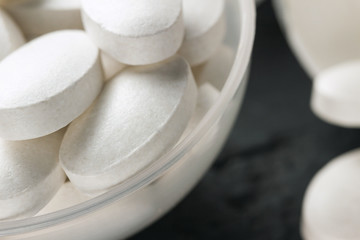 White medical supplement pills in the plastic spoon on dark background, macro image