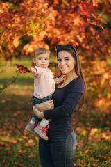 Obraz premium Mother with her little baby girl stand in front of red tree. Autumn park