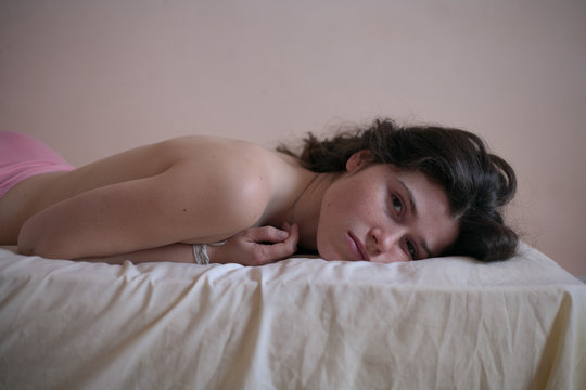 sad girl portrait with freckles without clothes on a bed with loose black hair