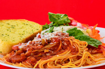 Closeup of Spaghetti with Garlic Bread and Salad on Red Background with Copy Space