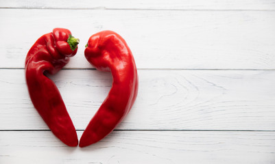 Two ugly red sweet peppers piled in a heart bud on a white wooden table. Copy space