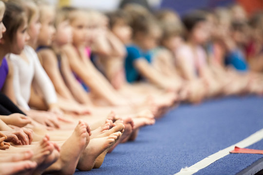 Children Barefoot Legs, Beginner Gymnasts Of Three And Four Old Ages Sitting In Line In A Sport School