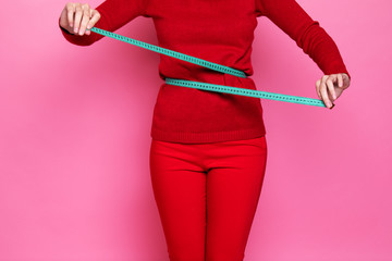 a girl in a red sweater and red pants measures her waist with a centimeter tape measure. the figure...