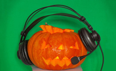 Pumpkin on a green plain background for Halloween with glowing eyes nose and mouth listening to the radio