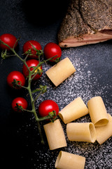 Paccheri pasta, Guanciale and cherry tomatoes on black background