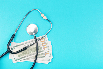 Stethoscope and dollar bills on blue background. Mock-up with copy space for your text. Concept of health care costs and medical expenses, saving money for health insurance. Flat layout, top view.