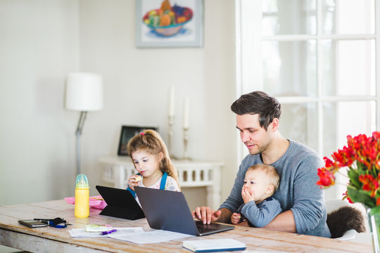 Mid adult man working on laptop while sitting with children at table